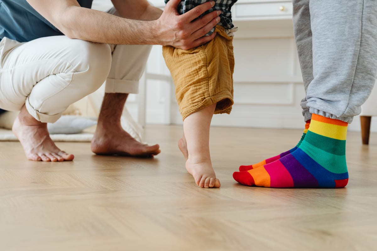 A toddler takes first steps with help from father indoors, showcasing love and support.